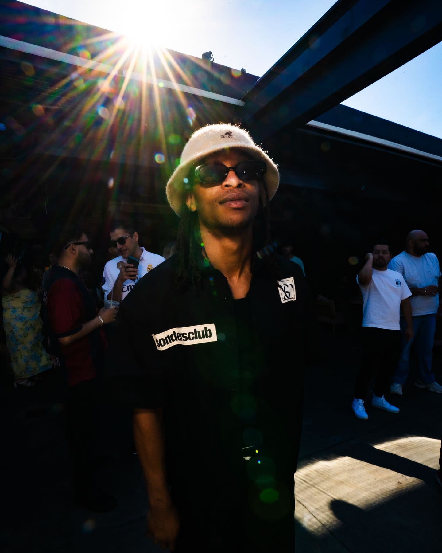 A DJ in a bucket hat with the sun flaring behind him